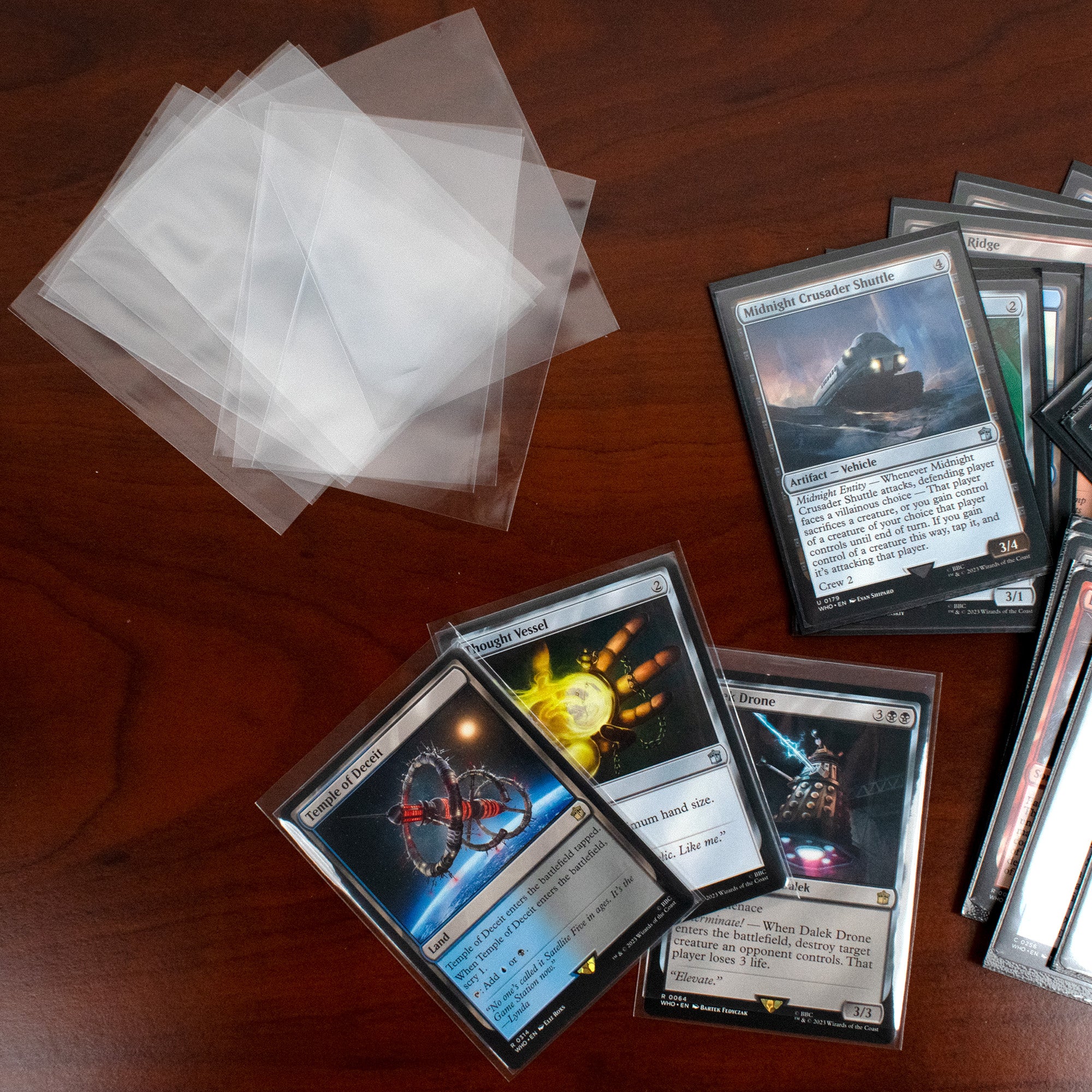 Collection of trading cards on a wooden surface with protective sleeves.